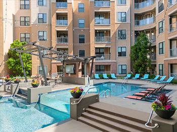 A large swimming pool with a slide and lounge chairs in front of apartment buildings.